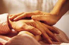La mano di una persona giovane è poggiata sulle mani incrociate di una persona anziana.