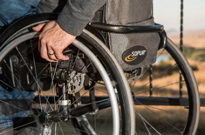 Un particolare della parte posteriore di una sedia a rotelle sulla quale è seduto un uomo con disabilità motoria.