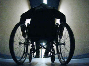 Una persona con disabilità motoria ritratta di spalle mentre si sposta, con la sedia a rotelle, lungo un corridoio.