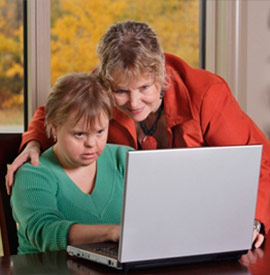 Una caregiver insegna una giovane donna con sindrome di Down ad usare il computer.