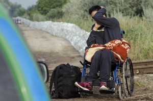 Una persona con disabilità motoria immigrata porta con sé una coperta ed uno zaino.