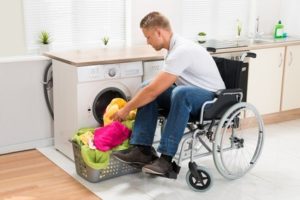 Un giovane uomo in sedia a rotelle infila i panni dentro la lavatrice.