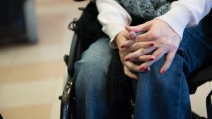 Le mani smaltate di una ragazza con disabilità motoria intrecciate sulle sue gambe.