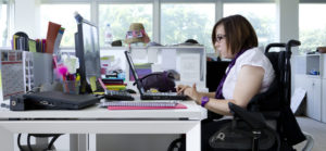 Una donna con disabilità motoria in un ufficio, mentre lavora al computer.