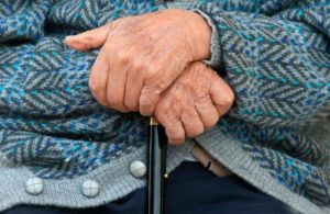 Le mani di una persona anziana poggiate su un bastone.