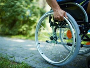 Un primo piano della ruota di una sedia a rotelle. Su di essa la mano della persona con disabilità che vi è seduta sopra.