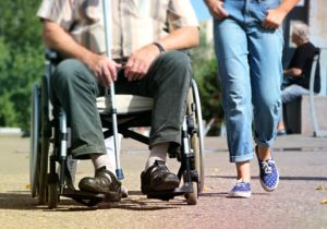 Le gambe di due persone che camminano assieme, una di esse si sposta in sedia a rotelle.