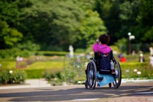 Una bambina con disabilità motoria, ritratta di spalle mentre scatta una foto ad un giardino.