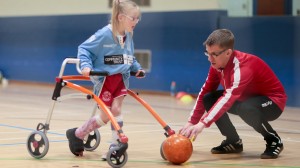Una bambina con disabilità motoria gioca a pallone. 