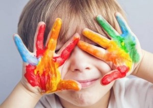 Un bambino autistico si copre il viso con le mani sporche di colori diversi.