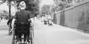 Una donna in sedia a rotelle ritratta di spalle in un percorso pedonale.