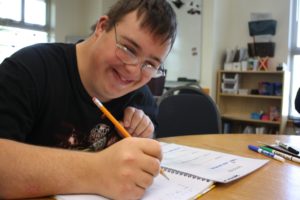 Un giovane con disabilità intellettiva scrive su un quaderno.