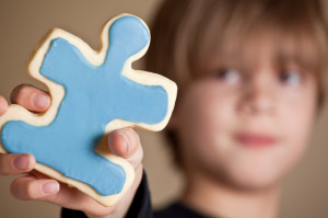 Il pezzo di un puzzle è retto dalla mano di un bambino, il cui viso rimane sullo sfondo e fuori fuoco. 
