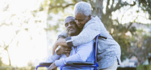 Una caregiver abbraccia un uomo con disabilità motoria.