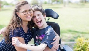 Un giovane con disabilità motoria abbraccia sorridente la sua assistente personale.