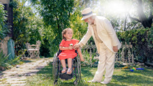 Un fotogramma tratto dal video realizzato dalla UILDM per la propria campagna lasciti mostra un signore che regala un fiore ad una bambina in sedia a rotelle.