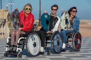 Tre persone con disabilità indossano e mostrano i copriruota realizzati da Vanity Wheel (fonte: pagina Facebook Vanity Wheel).