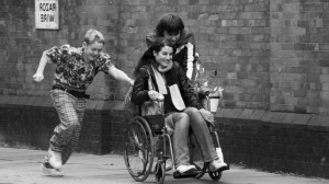 Una ragazza con disabilità motoria va in giro con due amici che si divertono a spingere la sua sedia a rotelle.