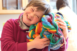 Una giovane donna con sindrome di Down sorride mentre stringe a sé una matassa di fili colorati.