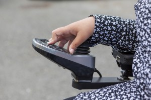 Una mano femminile gestisce il joystick di una sedia a rotelle elettrica. 