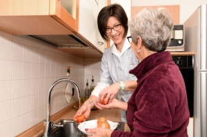 Una donna anziana lava dei pomodori col supporto di un’assistente domiciliare. 