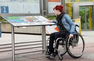 Una giovane donna con disabilità motoria consulta la mappa di una struttura situata su un apposito pannello.