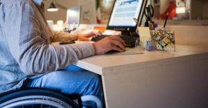 Particolare di un lavoratore in sedia a rotelle che lavora al computer. 