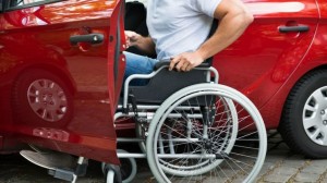 Particolare di una persone con disabilità motoria che entra in una macchina rossa.